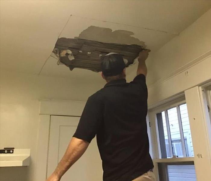 image of SERVPRO worker removing drywall from affected ceiling due to water damage