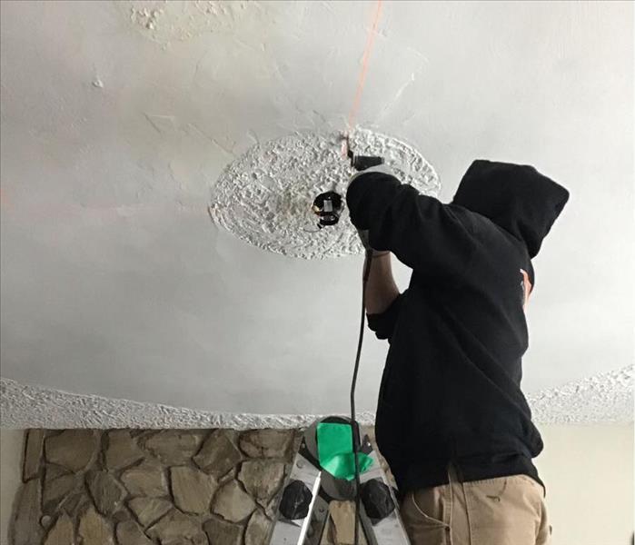 SERVPRO team member on a ladder is cutting out a ceiling.